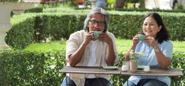 Afiş üst düzey çift ev bahçesinde kahve yudumlarken gülüyor.