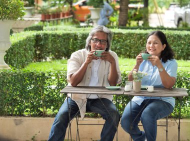 Afiş üst düzey çift ev bahçesinde kahve yudumlarken gülüyor.