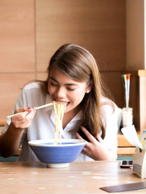Restoranda öğle yemeği zaman kavramı noodle yemek için yemek çubukları kullanarak mutlu Asyalı kadın kapatmak.