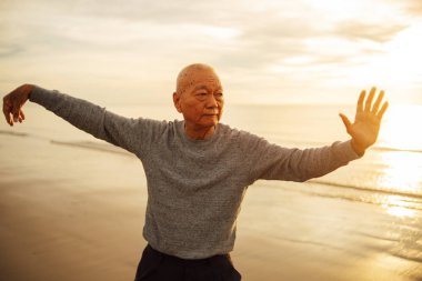 Asian Senior old man practice Tai chi and Yoga pose on the beach clipart