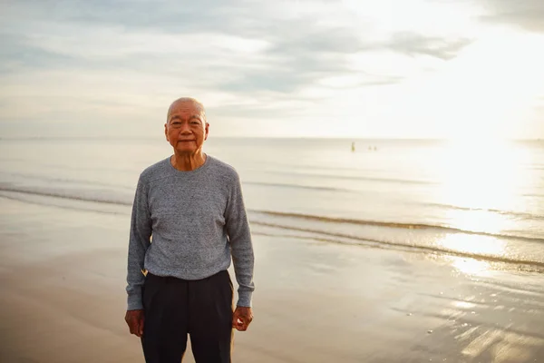 Старший азиатский мужчина практикует тайцзи и йогу позы на пляже — стоковое фото