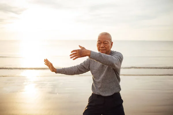 Asiatico anziano uomo anziano pratica Tai chi e Yoga posa sulla spiaggia — Foto Stock