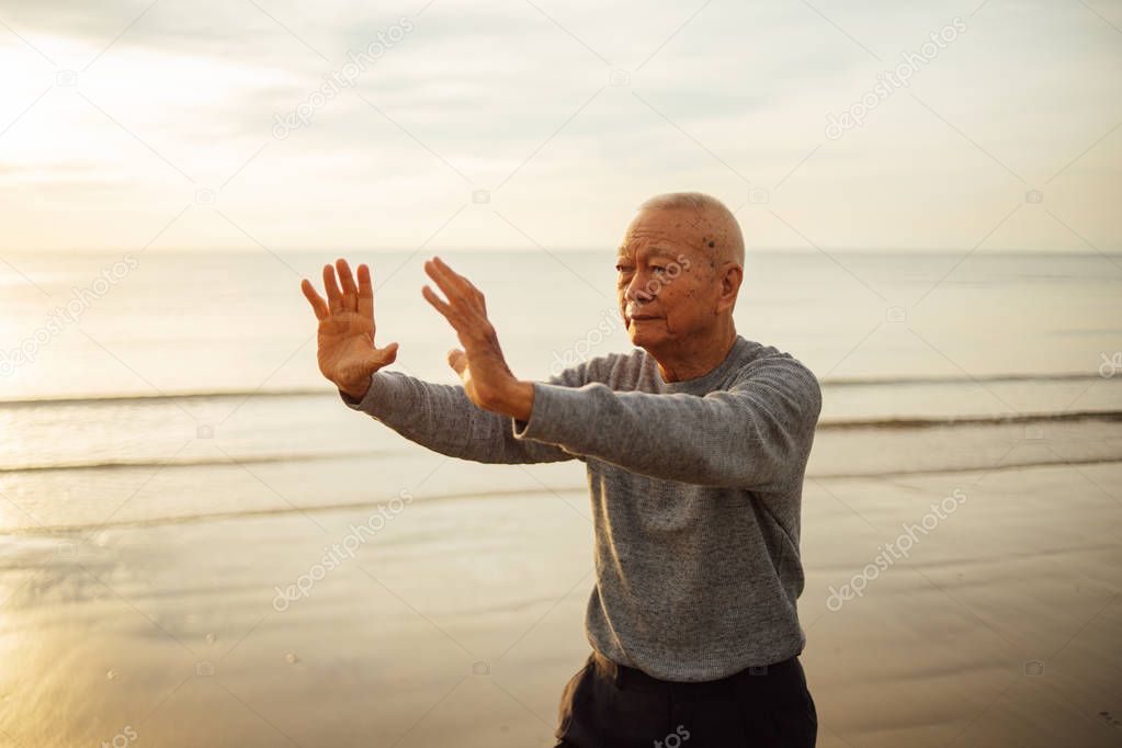 Asian Senior old man practice Tai chi and Yoga pose on the beach