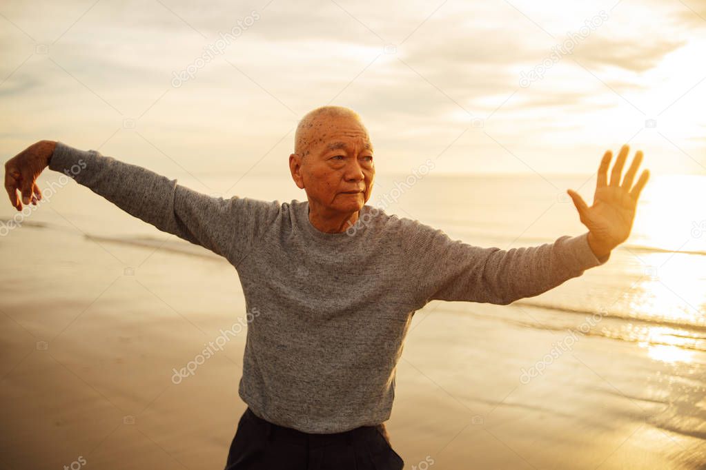 Asian Senior old man practice Tai chi and Yoga pose on the beach