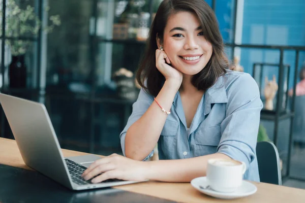 Asian woman in blue shirt  in cafe drinking coffee and using lap — Stock Photo, Image