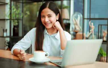 Mavi gömlekli Asyalı kadın çalışıyor ve kahve sho kahve içmek