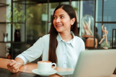 Mavi gömlekli Asyalı kadın çalışıyor ve kahve sho kahve içmek