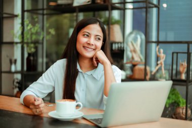 Mavi gömlekli Asyalı kadın çalışıyor ve kahve sho kahve içmek
