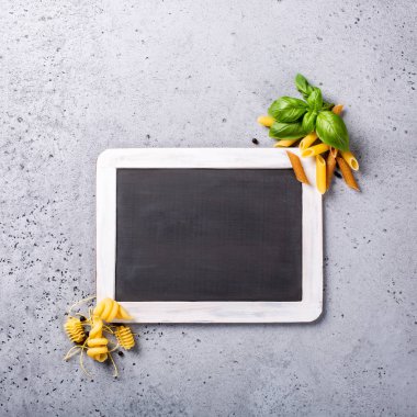 İtalyan makarna tam tahıl penne, trottole ve fesleğen ile siyah kara tahta gri beton masada bırakır. Menü, kafe, Restoran gıda arka plan kavramı. Uzay kopyalayın, yatıyordu, en iyi görünüm düz.