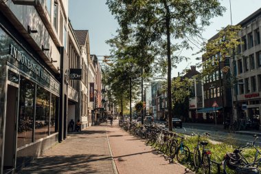 Eindhoven, Hollanda - 21 Eylül 2024: Parlak güneş ışığı altında dükkanların yanına parketmiş bisikletli canlı şehir caddesi
