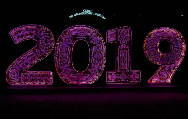 Violet led light numerals depicting new year of 2019 in Moscow Medvedkovo district at night. Russian led light text on the background: square on Olonetskiy passage.