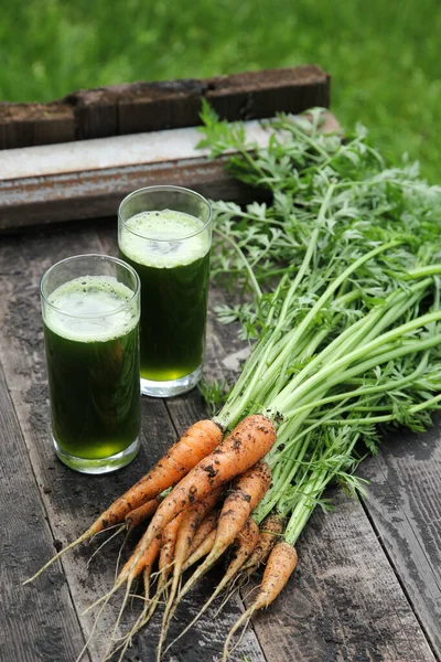 Drinks. Green smoothie from carrot tops in a glass. A bunch of carrots on an old wooden background. Rustic. Background image, copy space