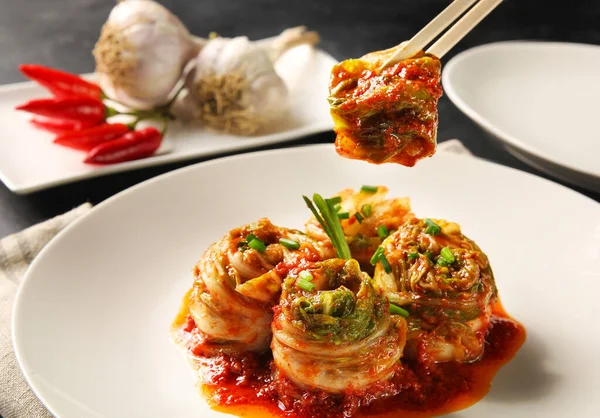 The Korean national cuisine. Peking cabbage kimchi roll with vegetables, red sauce, green onion, garlic  and chili pepper on a white plate on a black background. Horizontal. Background image