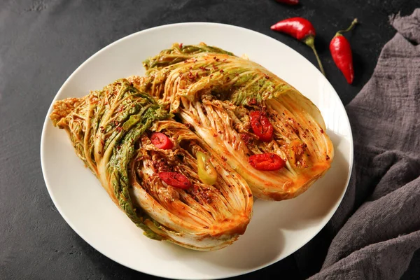 The Korean national cuisine. Peking cabbage kimchi with vegetables, red sauce and chili pepper on a white plate on a black background. Horizontal. Background image, copy space