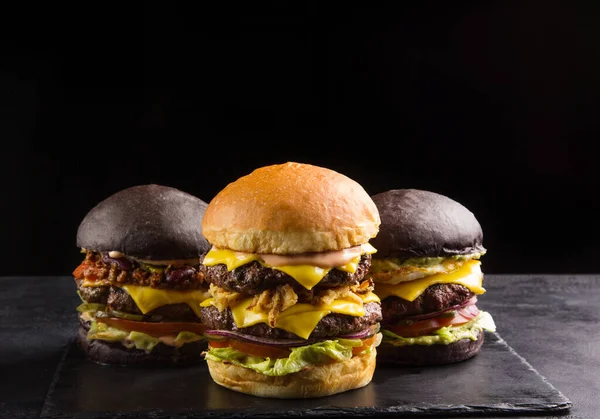 Fast food. American cuisine. Double cheeseburger and black burgers. Burger with beef cutlet, onion, cheese, lettuce and tomato on black board. Background image, copy space