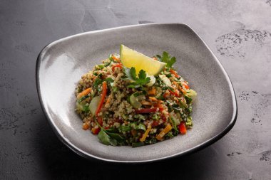 Sebzeli, şifalı ve limonlu kinoa. Siyah arka planda gri bir tabakta havuçlu, kerevizli, biberli ve maydanozlu lapa.