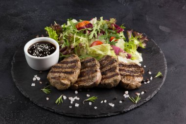 Soslu ızgara et ve ot salatası, roka, siyah arka planda kara tahtada vişneli domates. Arkaplan resmi, alanı kopyala