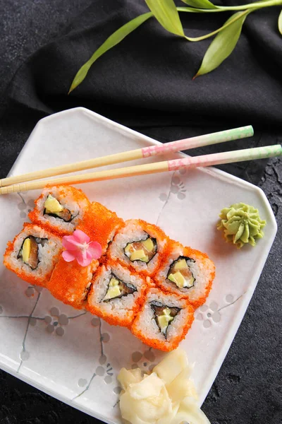 Japanese cuisine. Rice rolls with red caviar and wasabi on a white plate on a black table with chopsticks. Restaurant menu. Background image, copy space, flatlay