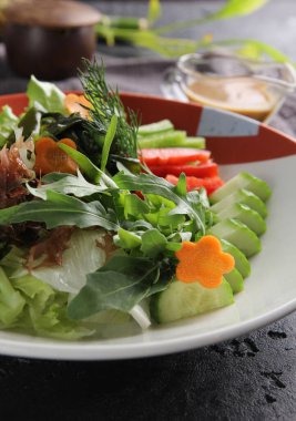 Japon mutfağı. Çiğ sebzeler: salatalık, biber, havuç ve brokoli. Arugula, marul, dereotu ve sos yemek çubuklarıyla siyah bir masada. Arkaplan resmi, kopyalama alanı, düz alan