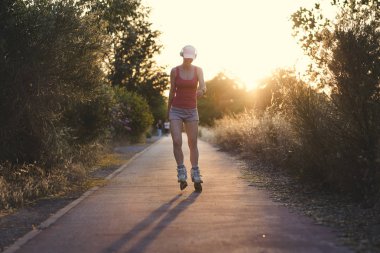 Genç kadın açık havada günbatımı sırasında paten yaparken eğlenmek. Çekici erkek bir soluk pembe kap ve müzik onun kulaklıklar ile egzersiz yaparak spor giysiler giyiyor.