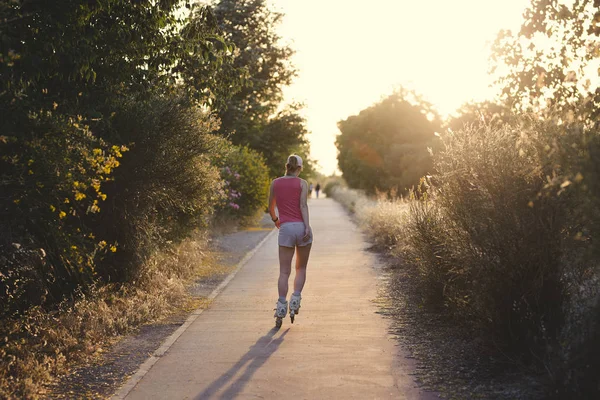 Genç kadın açık havada günbatımı sırasında paten yaparken eğlenmek. Çekici erkek bir soluk pembe kap ve egzersiz yaparak spor giysiler giyiyor