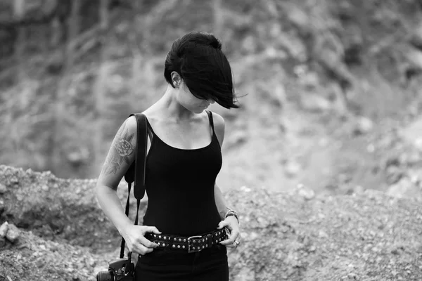professional photographer outdoors with stone texture background.  Black and white portrait of beautiful young woman with her dslr camera wearing black clothes.