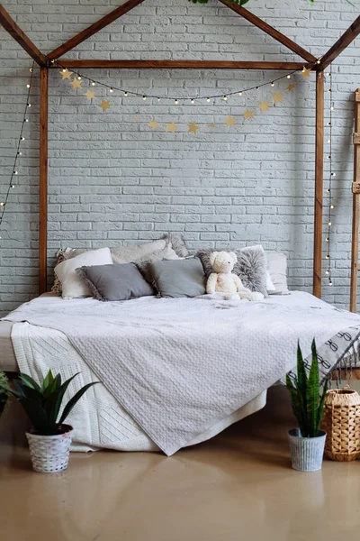 Modern bedroom interior with plants, pillows and teddy bear on bed