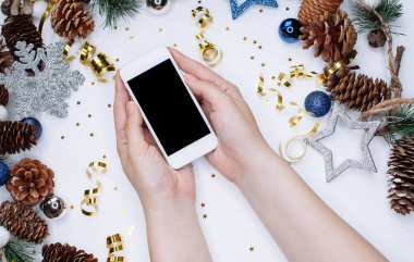 Erkek Noel koniler, kar taneleri ve konfeti ile beyaz arka plan üzerinde akıllı cep telefonu tutan eller. Düz yatıyordu kompozisyon üstten görünüm.