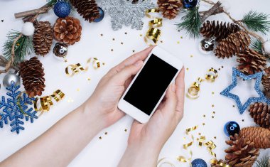 Erkek Noel koniler, kar taneleri ve konfeti ile beyaz arka plan üzerinde akıllı cep telefonu tutan eller. Düz yatıyordu kompozisyon üstten görünüm.