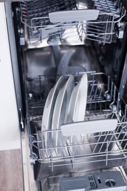 Bulaşık makinesini beyaz mutfakta temiz bulaşıklarla açın.