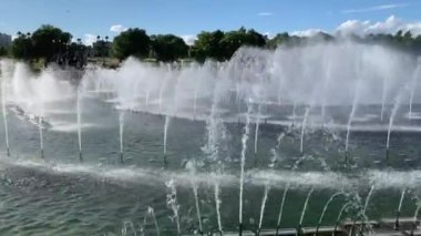 Yaz günü şehir parkının ortasına su fışkırtan fıskiyeler. Mavi açık gökyüzü. 