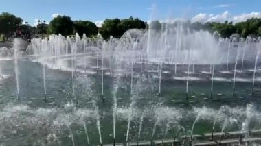 Yaz günü şehir parkının ortasına su fışkırtan fıskiyeler. Mavi açık gökyüzü. 