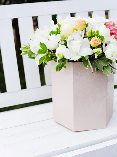 White box with flower bouquet on bench.