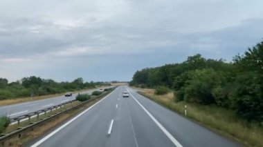  Almanya 'da otoyol. Asfalt yolu, renkli ağaçlar, güneşli gökyüzü. Araba yolculuğu, ikinci kat otobüs durağı.