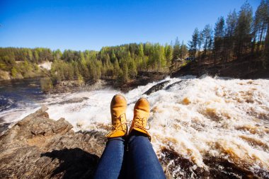 Kot pantolonlu ve açık kahverengi çizmeli bir kadın oturuyor.