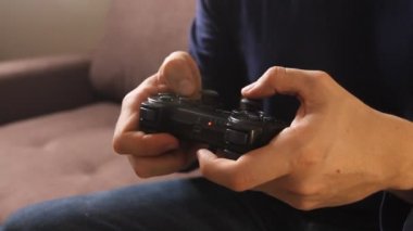 Kanepede oturmuş oyun konsolunda video oyunu oynayan adamın elleri yakın plan.