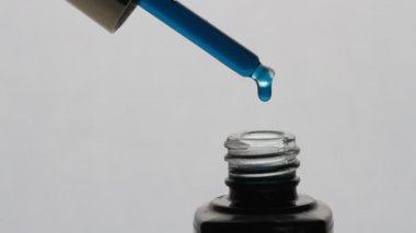 Mavi yağ damlalarının beyaz arka planda, pipetten düşüşü. Şişeye, kozmetolojiye ve sağlık hizmetlerine yağ damlatan damlalar.