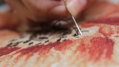 Kadın elleri kırmızı çiçeğe çapraz dikiş atıyor. Kapalı bir nakış..