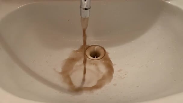 バスルームのシンクでタップから流れる汚れた錆びた茶色の汚染された水を閉じます — ストック動画