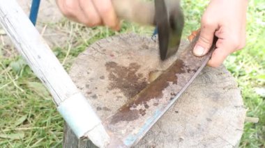 Çekiçle tırpanlayan bir adam. Tırpanı elle keskinleştirmek, kırsal bir alan.