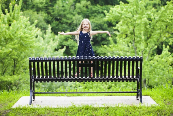 Portrait of happy little girl standing on metal bench in park — Stock Photo, Image