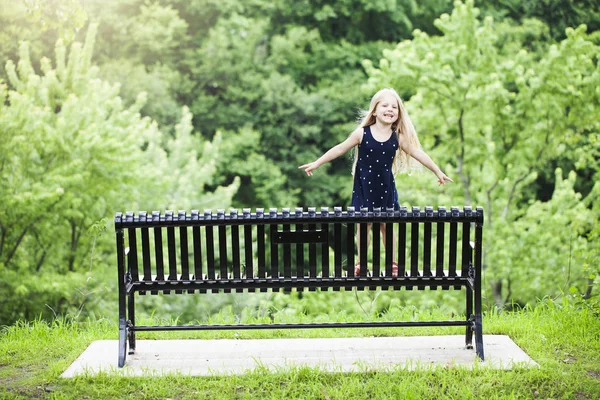 Portrait of smiling little girl standing on bench outdoors — Stock Photo, Image