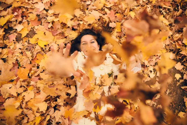 Mujer joven feliz acostada en el follaje y lanzando hojas de otoño — Foto de Stock