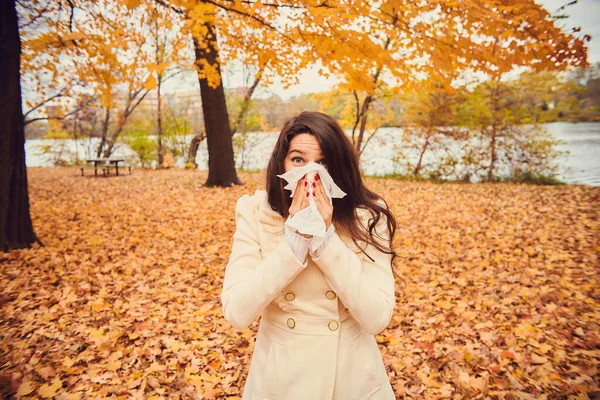 Retrato de una mujer joven sonándose la nariz en el parque de otoño — Foto de Stock