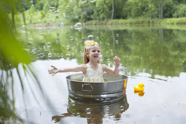 Smiling little girl floating in metal tub in park — Stock Photo, Image