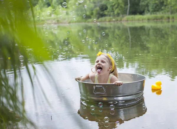 Excited girl sitting in tub and sticking out tongue at lake — Stock Photo, Image