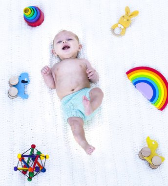 Oyuncaklarla beşikte yatıp gülen küçük bir çocuk.