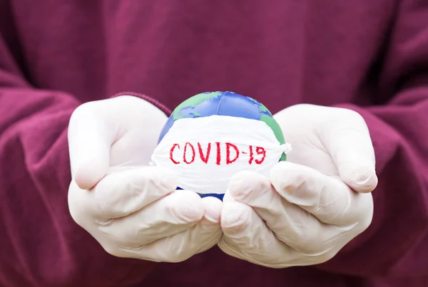 Stop corona virus. Conceptual photo of female hands in medical gloves holding globe with face mask on it