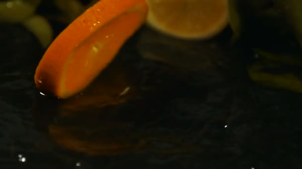 Orangenscheiben Fallen Auf Wasseroberfläche Mit Spritzer Auf Schwarzem Hintergrund Nahaufnahme — Stockvideo