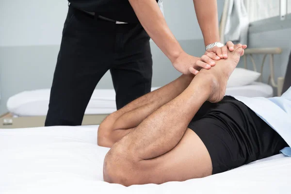 理学療法士は 医療室のベッドで横たわる患者の脚のハンドルを使ってください — ストック写真
